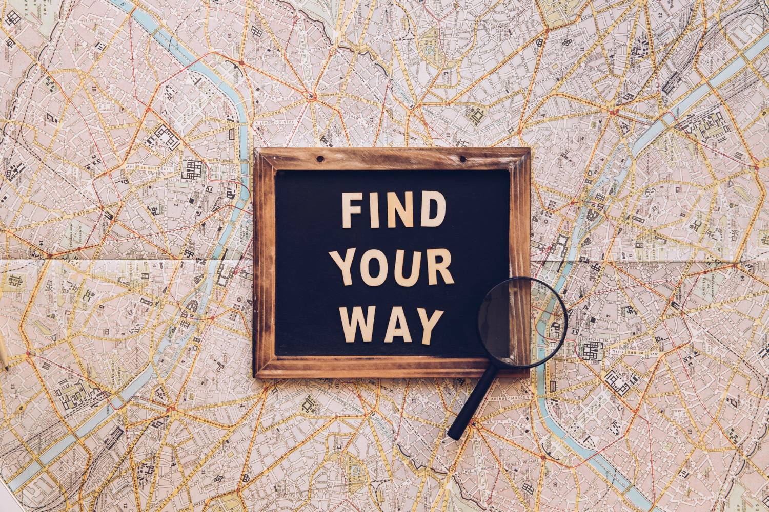 Chalkboard with 'FIND YOUR WAY' text over a detailed city map, magnifying glass nearby, symbolizing navigation and exploration.